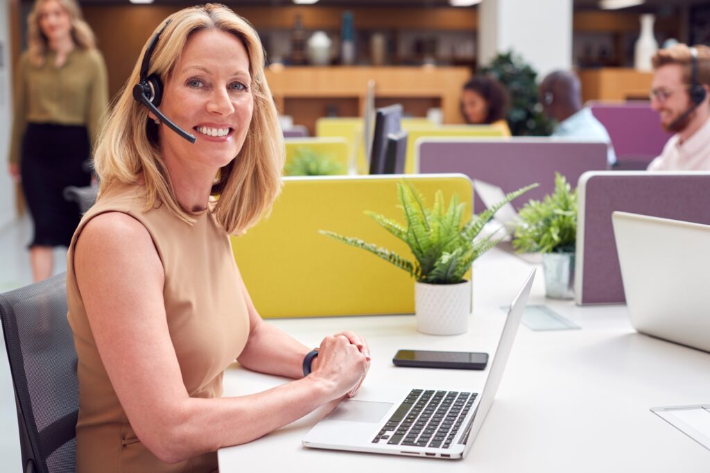 Portrait Of Mature Businesswoman Wearing Phone Headset Talking To Caller In Customer Services Centre